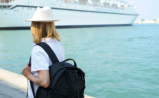 woman with backpack stands in front of cruise ship