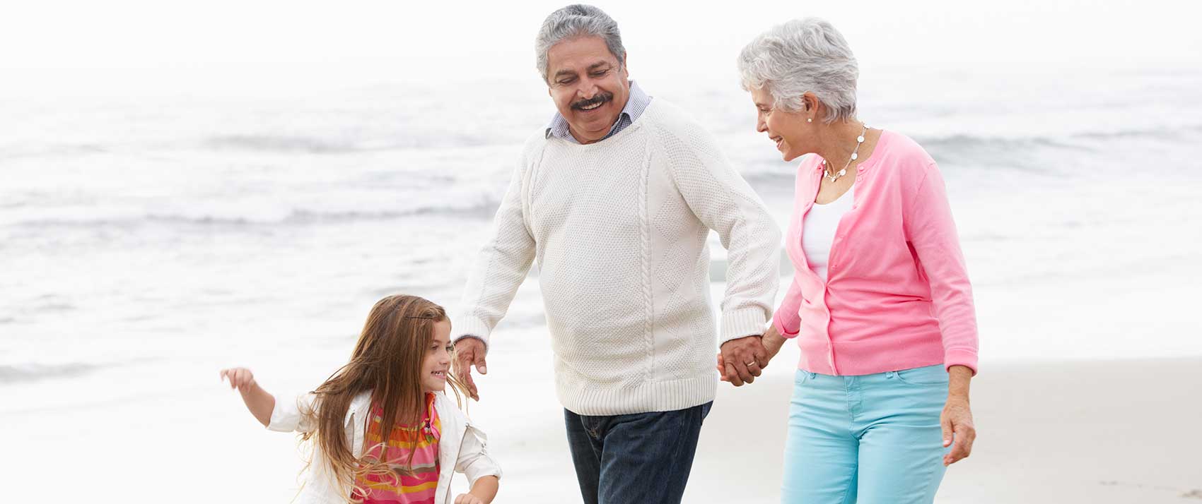 Grandparents walk on beach with grandchild